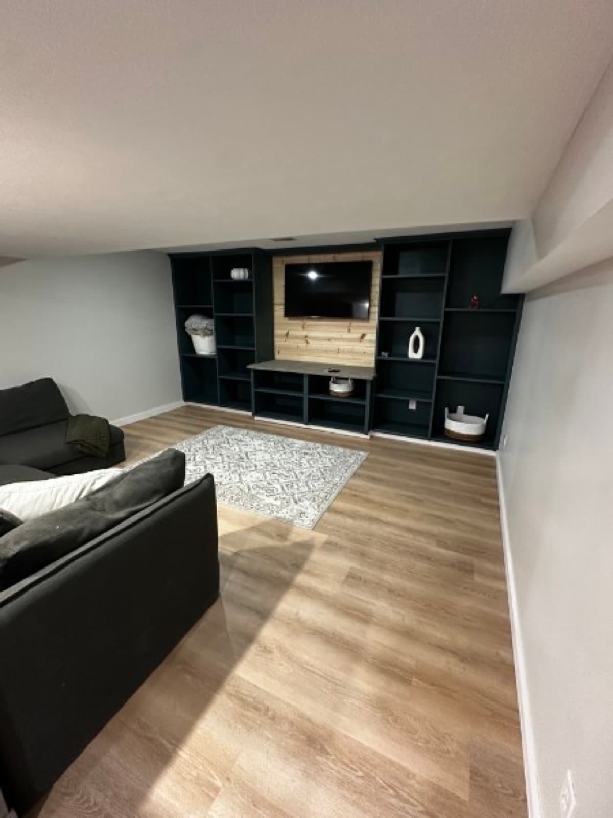 Finished basement built-in media wall in dark green with shiplap TV panel and LVP flooring
