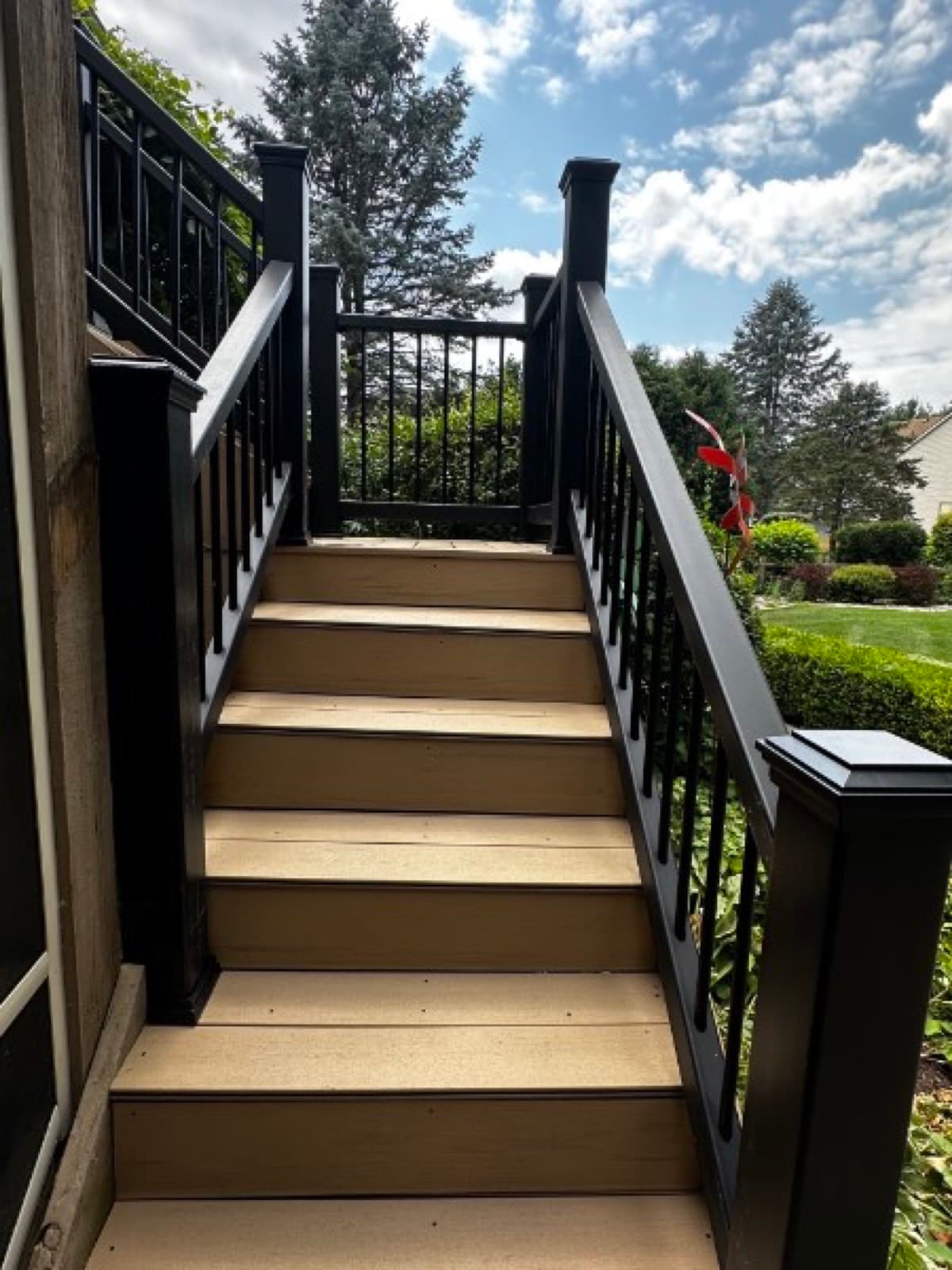 Composite deck staircase rising to a black aluminum gate under bright blue sky