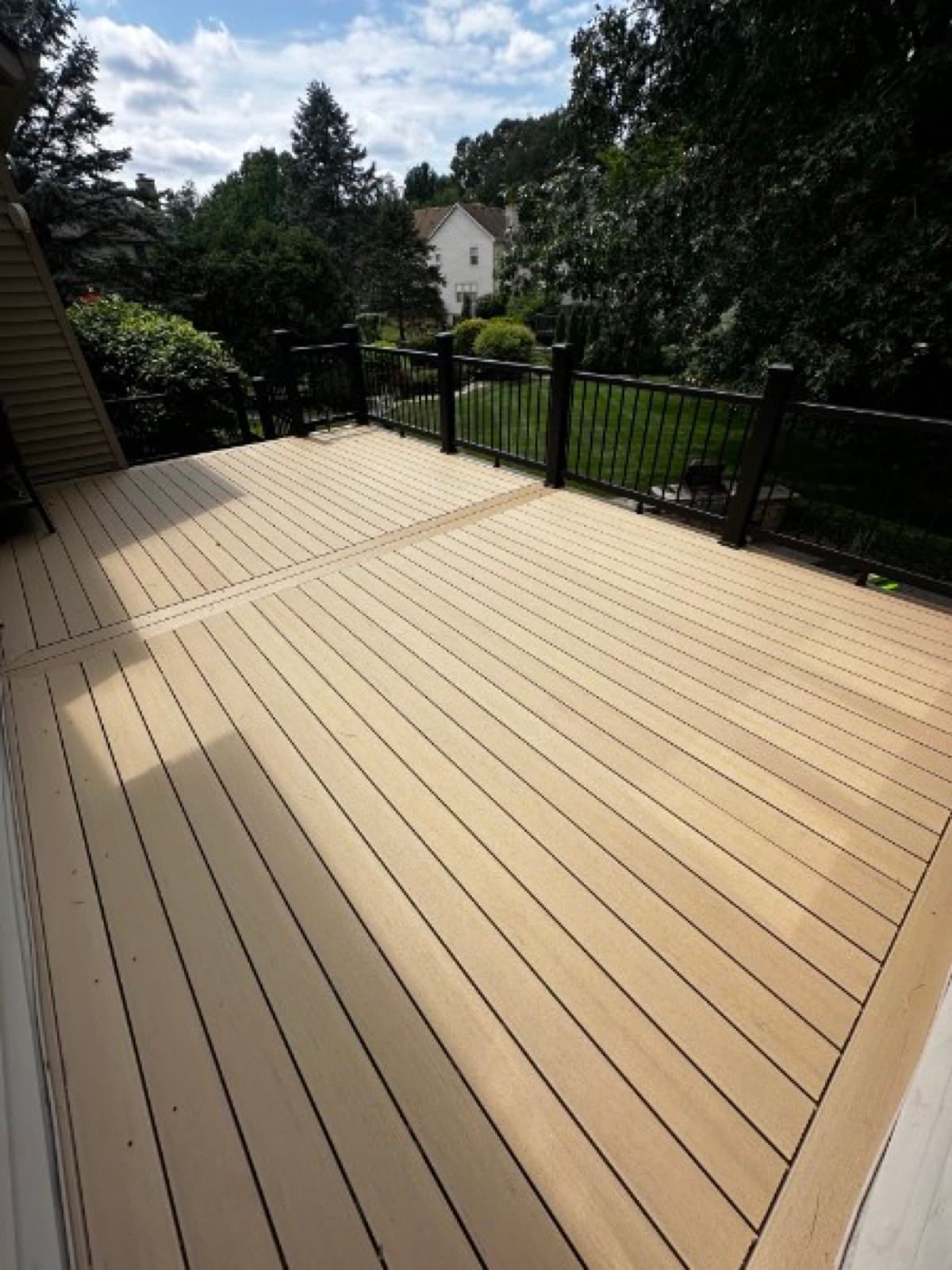 Finished khaki composite deck landing with black aluminum railing overlooking a wooded yard