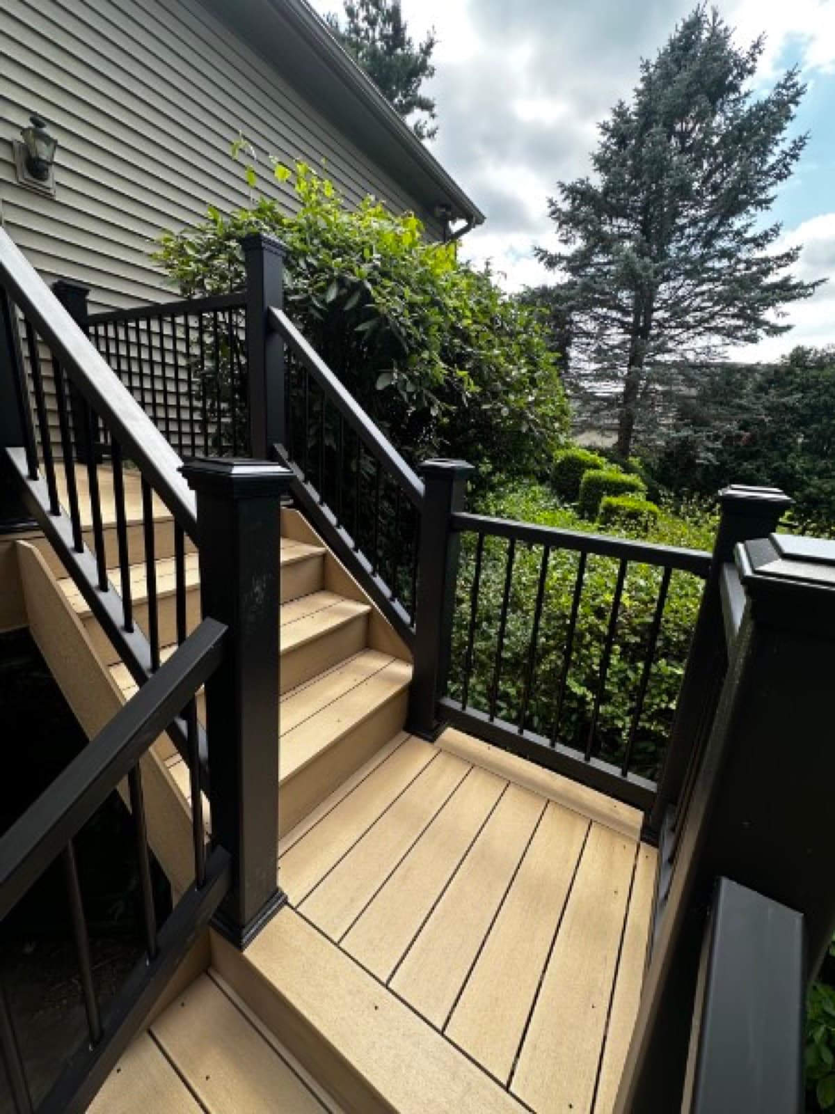 Mid-flight turn on a composite deck staircase with black metal balusters and lush greenery