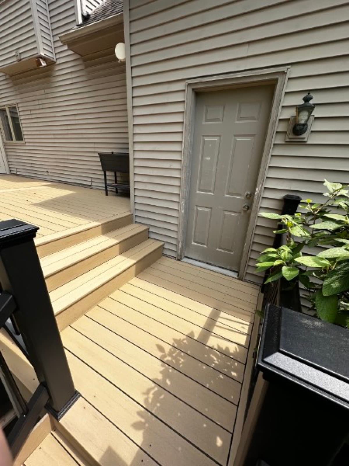 Looking down composite deck steps to a gray side-entry door under tan siding