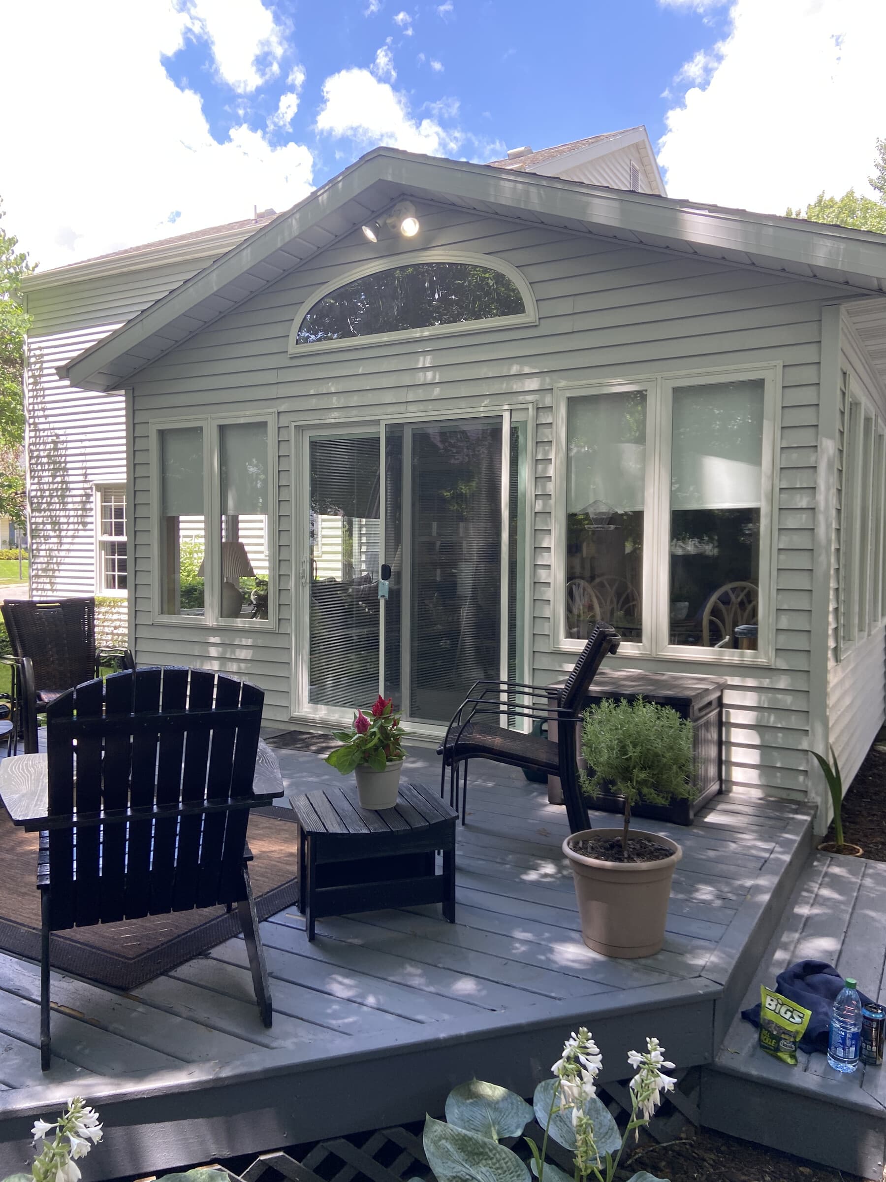 Green-grey home with new sliding door, arched gable window, Adirondack chairs, and lush hostas in summer light