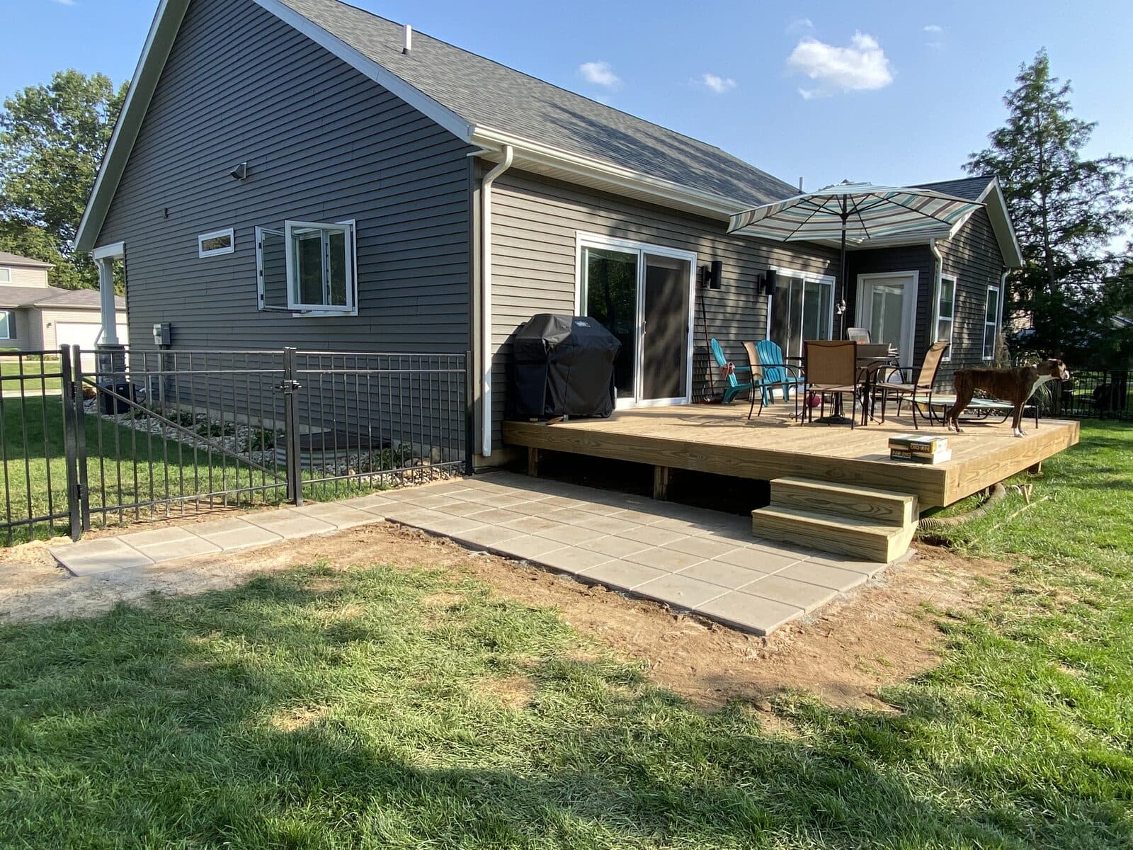 Finished wood deck with paver landing, patio set, and grill behind a gray home with fenced yard